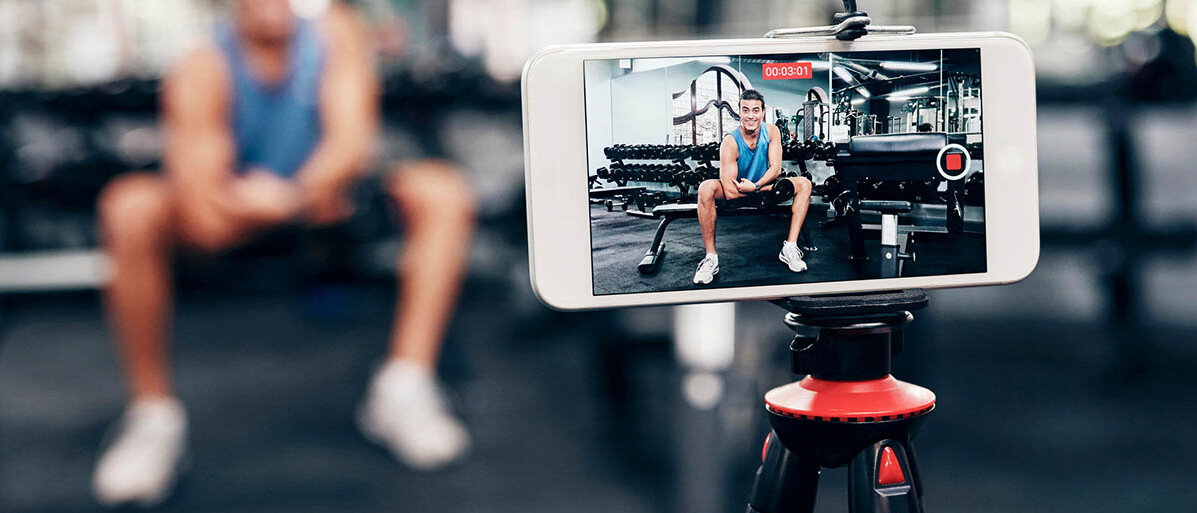Peptide als Spritze: Das ist die Wirkung und diese Risiken drohen. Ein muskulöser Mann im Fitnessstudio filmt sich dabei, wie er auf seinen Bizeps zeigt.