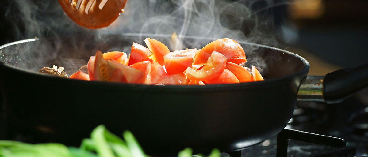 Aus einer Pfanne, in der Tomaten braten, steigt Dampf auf.