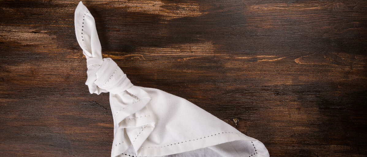 weißes Taschentuch mit einem Knoten liegt auf einem Holztisch