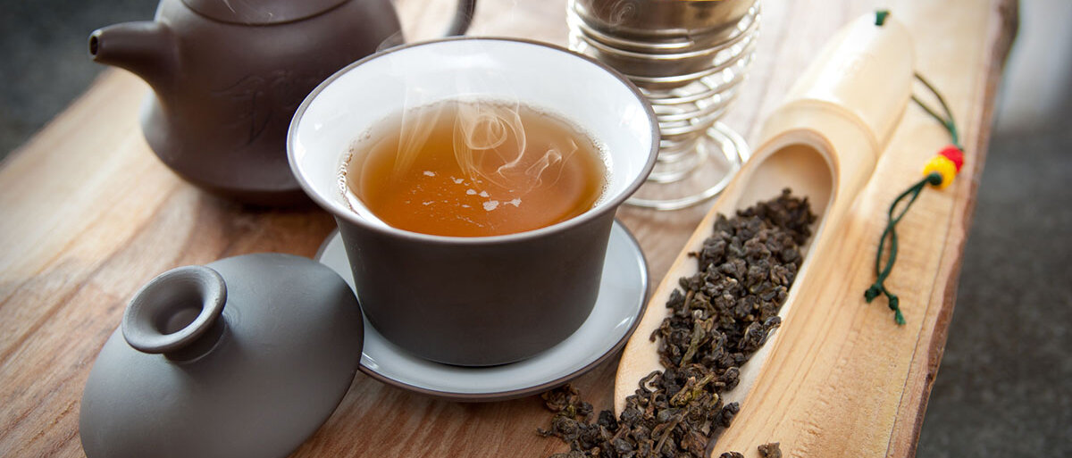 Teekanne, Teesieb, Teetasse gefüllt mit Tee, lose, gerollte, dunkle Teeblätter