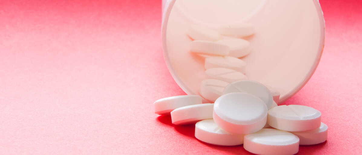 Weiße Medikamentendose aus der Tabletten fallen auf rotem Hintergrund