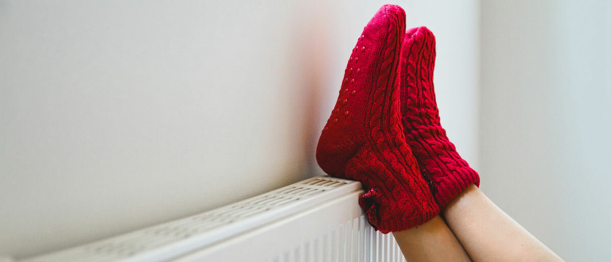 Frau mit roten Socken legt ihre Füße auf eine Heizung
