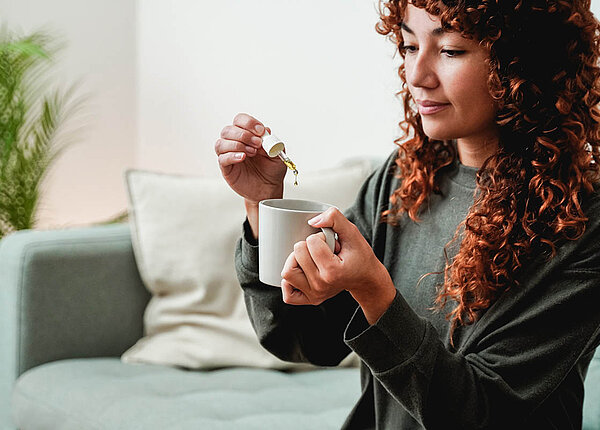 Eine junge Frau tropft Cannabis-Extrakt in ihre Tasse.