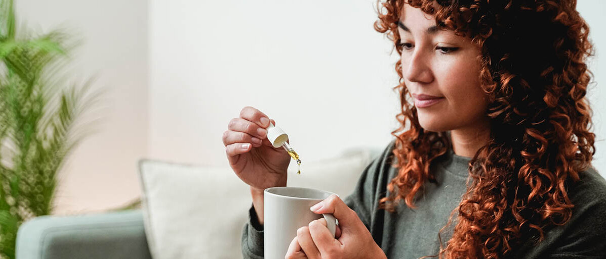Eine junge Frau tropft Cannabis-Extrakt in ihre Tasse.