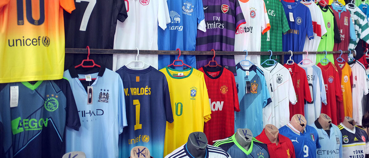 viele bunte Fußballtrikots hängen an einem Marktstand nebeneinander