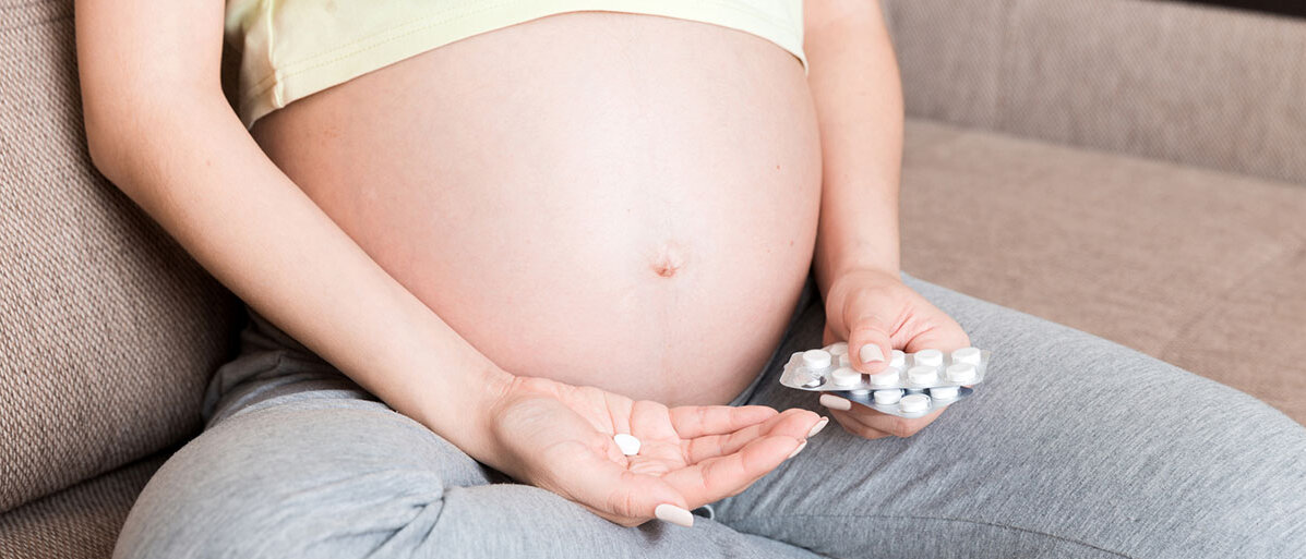 Schwangere Frau hält Paracetamol in der Hand.