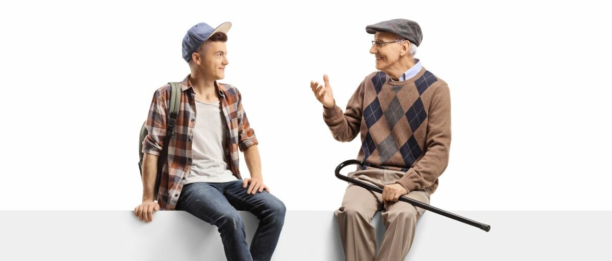Ein Senior und ein Jugendlicher sitzen auf einer Mauer vor weißem Hintergrund und unterhalten sich.
