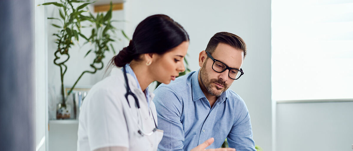 Wechseljahre bei Männern erkennen Gespräch der Gesundheitsergebnisse zwischen einem Mann und einer Ärztin, die auf einem Tablett zu sehen sind.