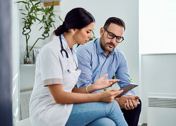 Gespräch der Gesundheitsergebnisse zwischen einem Mann und einer Ärztin, die auf einem Tablett zu sehen sind. 