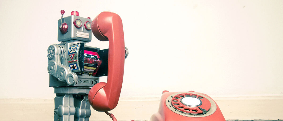 Ein Spielzeugroboter telefoniert mit einem alten, orangen Telefon mit Wählscheibe.