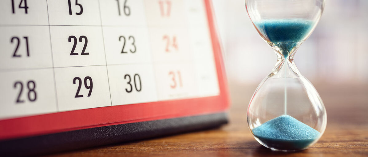Eine Sanduhr steht neben einem Kalender. Das Kalenderblatt zeigt das Ende des Jahres. Die Sanduhr läuft gerade durch.
