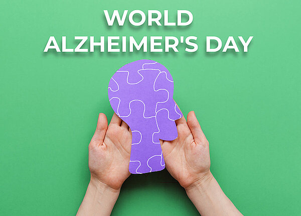 Gehirn als Puzzle gehalten von Frauenhänden auf grünem Hintergrund. Darüber steht Welt Alzheimertag