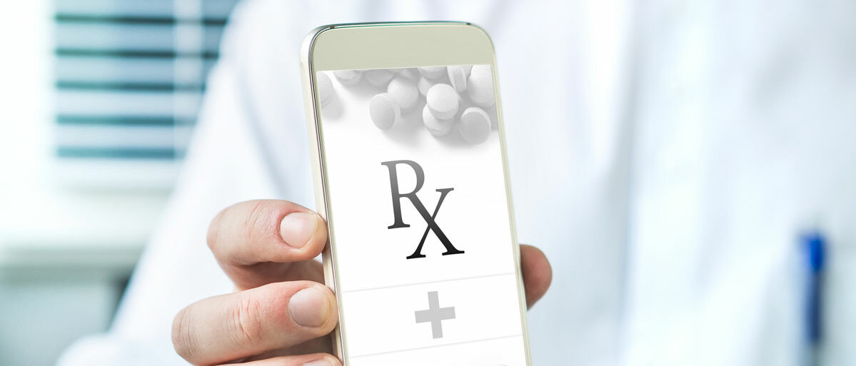 Ein Mann im weißen Kittel zeigt sein Smartphone, auf dem Display sind Tabletten und das Rx-Zeichen für "verschreibungspflichtig" zu sehen.