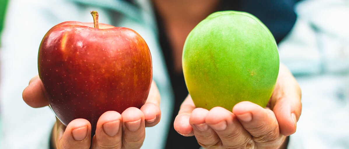 Jemand hält in jeder Hand einen Apfel. Einer ist rot und rund, der andere ovaler und grün.