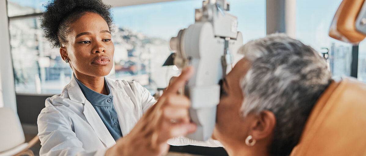 Junge Schwarze Optikerin prüft die Augen einer älteren Dame mit einem Gerät zur Sehmessung