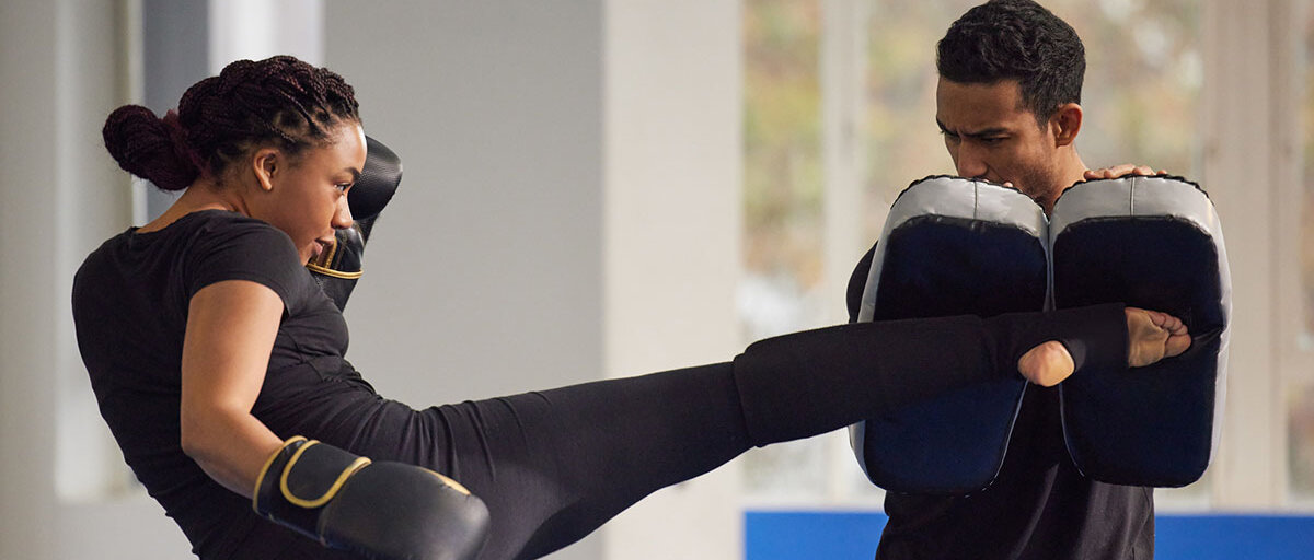 Eine Frau im Sportstudio tritt beim Kickboxen in Kissen, die ihr Trainingspartner hochhält.