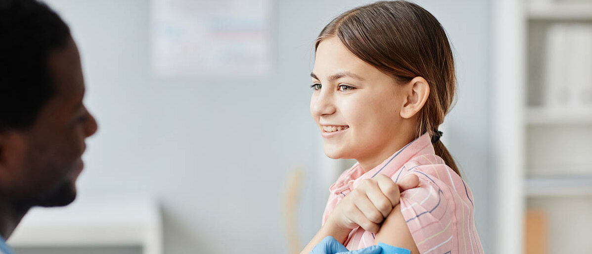 Ein Arzt klebt einer Teenagerin ein Pflaster auf den Oberarm.