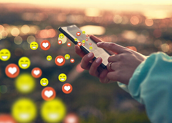 Soziale Medien Nutzung Soziale Medien werden auf einem Handy bedient, dabei fliegen lachende Emojis und Herzen aus dem Smartphone heraus.