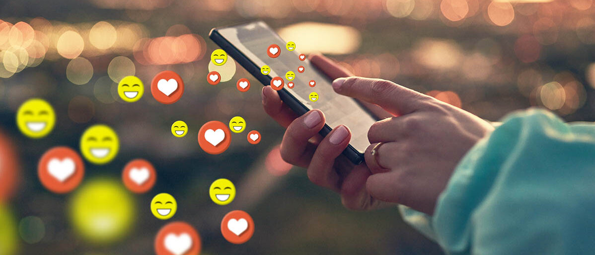 Soziale Medien Nutzung Soziale Medien werden auf einem Handy bedient, dabei fliegen lachende Emojis und Herzen aus dem Smartphone heraus.