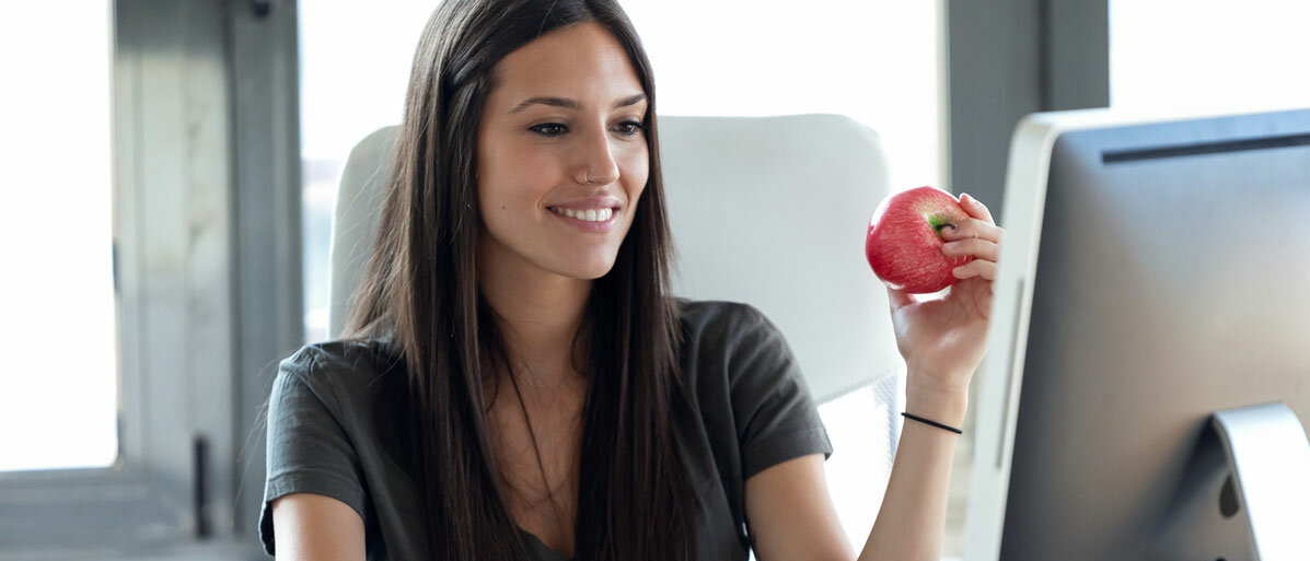 Junge Frau sitzt am Schreibtisch und isst einen Apfel