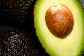 Aufgeschnittene Avocado mit Kern auf Schieferplatte, daneben Messer mit Klinge aus Stahl 