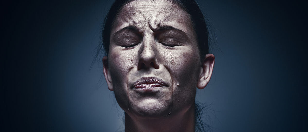 Eine Frau verzieht das Gesicht und weint.