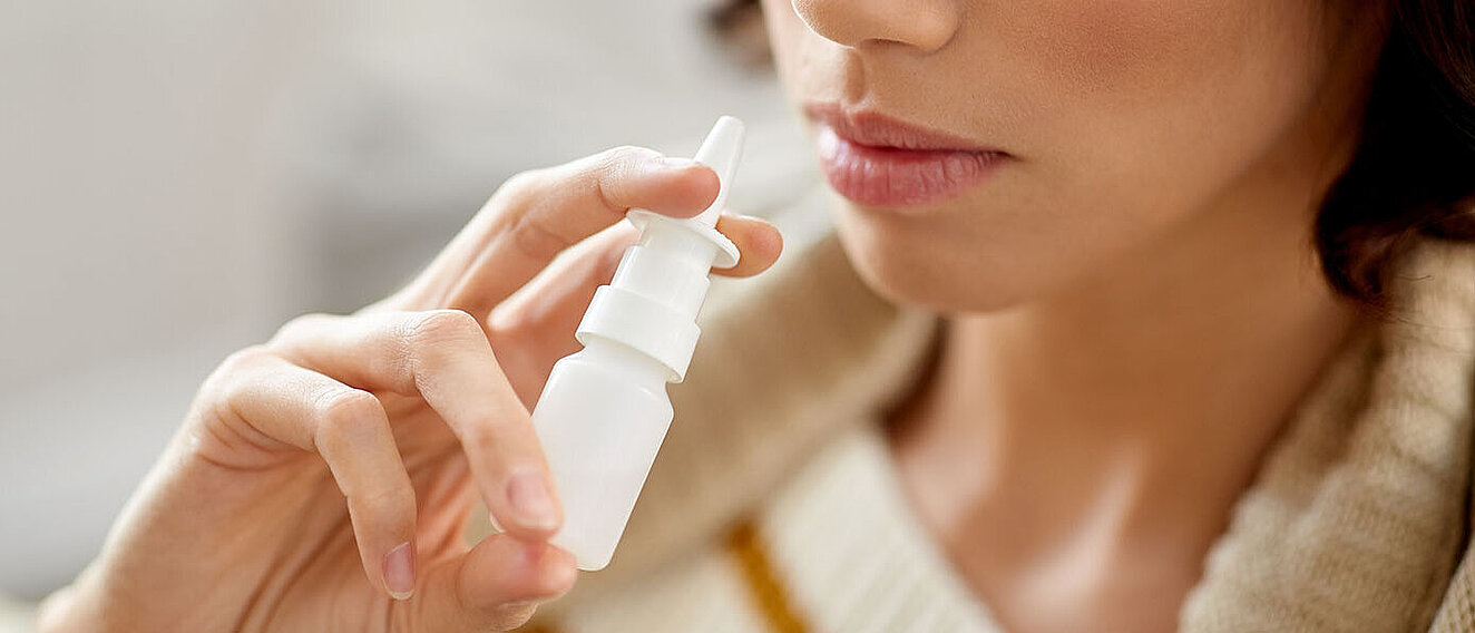Gesicht einer Frau, die sich mit einer Hand Nasenspray in die Nase sprüht