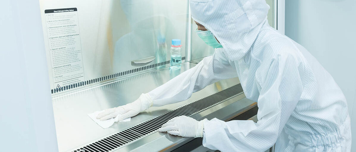 Sterile Augentropfen herstellen mit verschiedenen Sterilisationsverfahren: konservierte und unkonservierte Eine Frau in Schutzkleidung reinigt eine Laminar-Air-Flow-Bank.