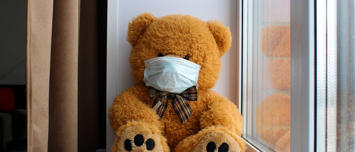 Ein Teddybär mit Mundschutz sitzt am Fenster