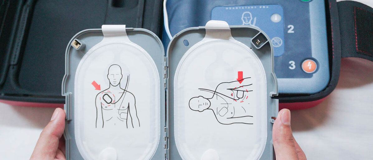 Jemand hat die Tasche eines automatischen externen Defibrillators geöffnet und hält die geöffnete Box mit den Klebepads in der Hand.