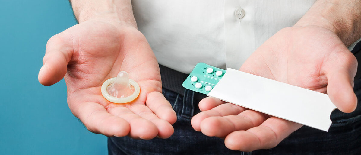 Mann hält ein Kondom in der linken Hand und ein Blister mit Pillen in der rechten Hand