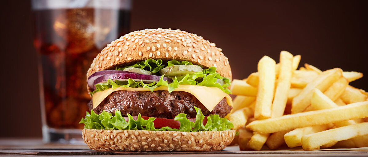 Cola, Burger und Pommes stehen nebeneinander auf schwarzem Hintergrund