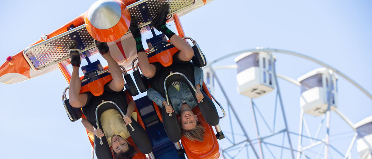 Zwei Menschen fahren auf dem Jahrmarkt mit einem Fahrgeschäft, gerade hängen sie kopfüber.