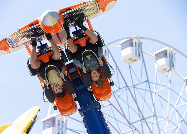 Zwei Menschen fahren auf dem Jahrmarkt mit einem Fahrgeschäft, gerade hängen sie kopfüber.