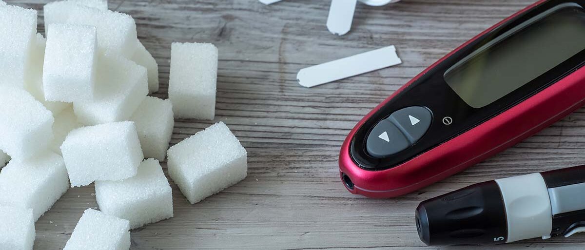 Zuckerwürfel und Diabetes-Messgerät mit Teststreifen auf einem Holztisch
