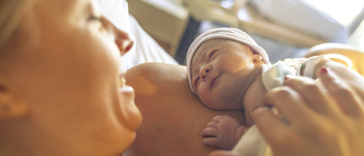 Ein neugeborenes liegt auf der Brust der Mutter und lächelt sie an