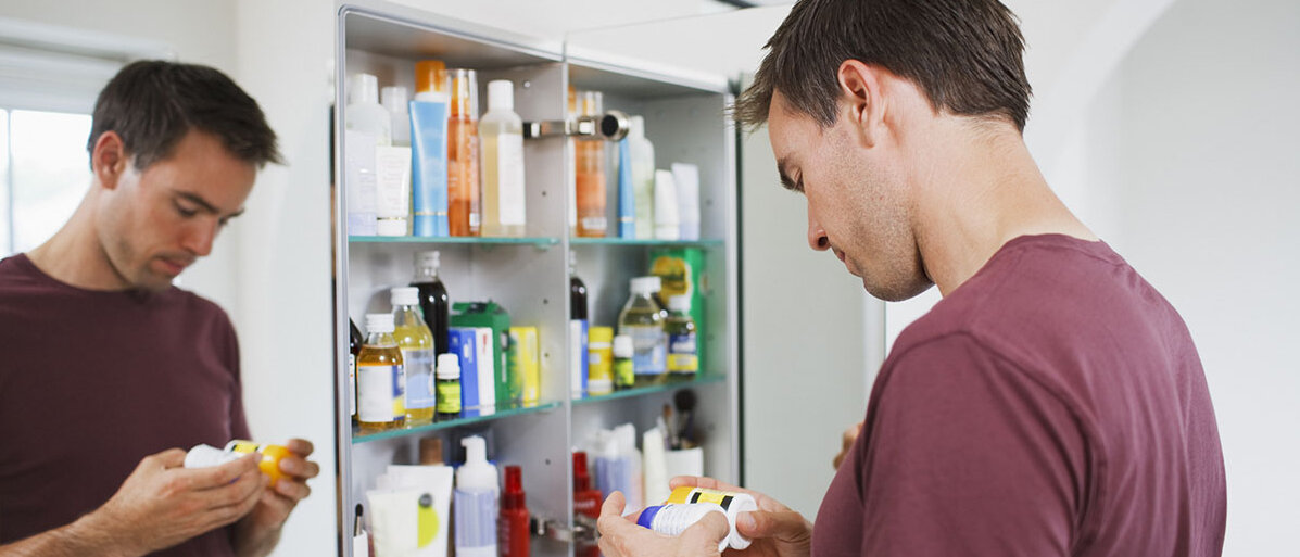 Mann checkt Medikamente vor offenem Badezimmer-Spiegelschrank