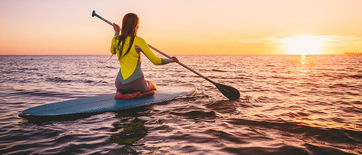 Frau Kniet auf Stand-up Paddling und hat ein Ruder in der Hand