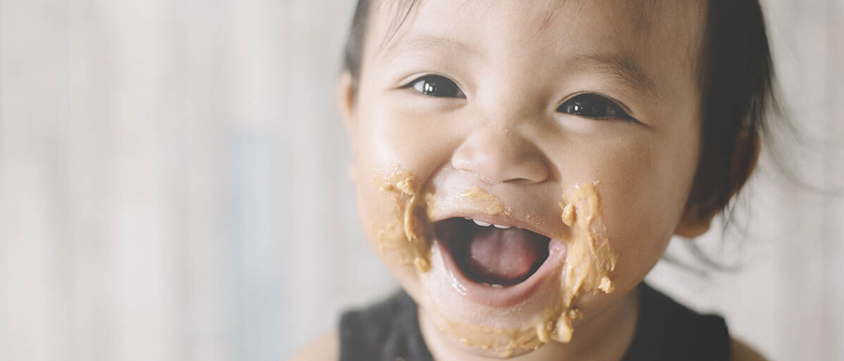 Lebensmittelallergie wie Erdnussallergie bei Kindern Ein Baby lächelt breit, sein Mund ist mit Erdnussbutter verschmiert.