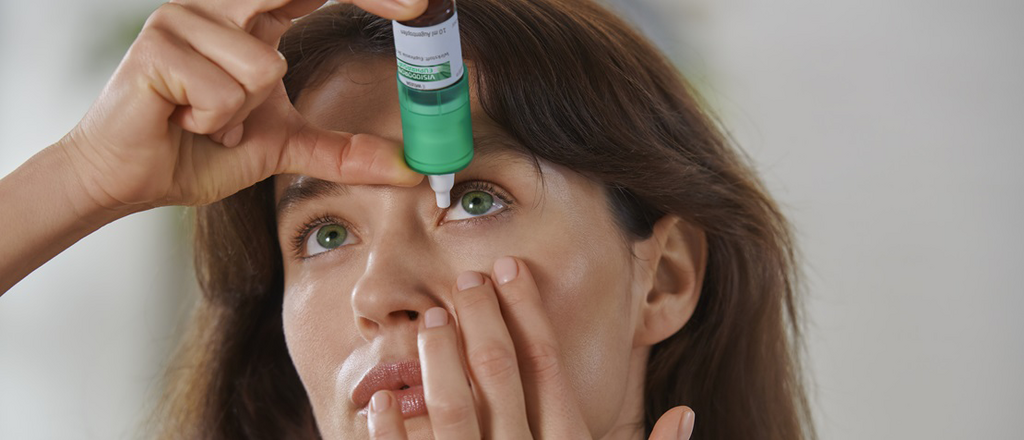 Eine Frau tropft sich Visiodoron Euphrasia® Augentropfen aus einem grün-weißen Mehrdosenbehältnis ins Auge.