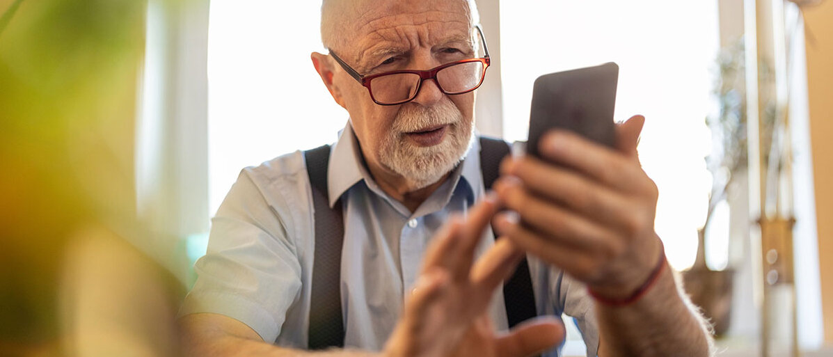 Älterer Mann starrt verwirrt auf sein Smartphone.