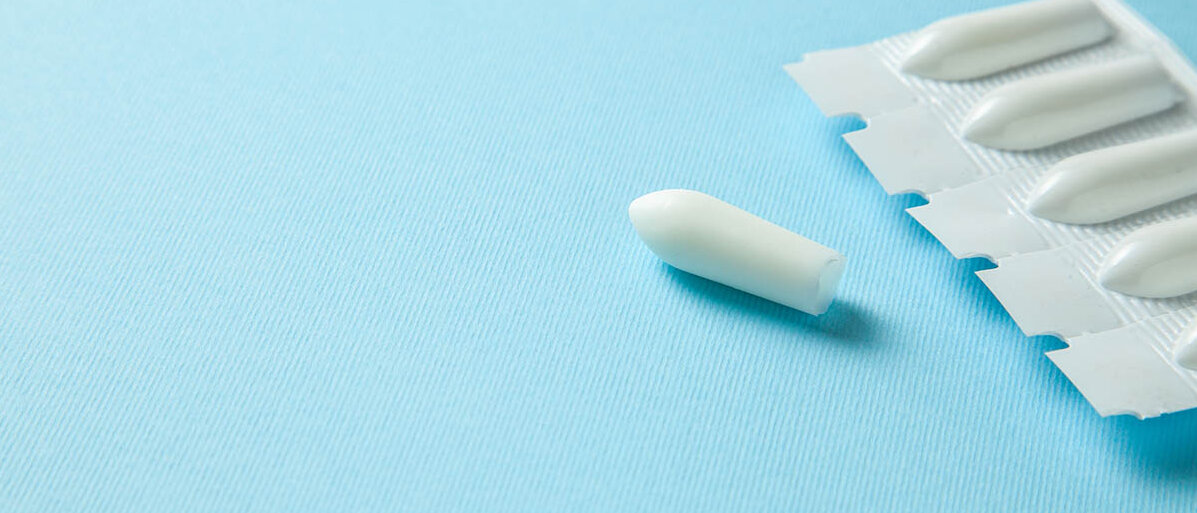 Ein Blister mit 5 Suppositorien sowie ein loses Zäpfchen liegen auf blauem Grund.