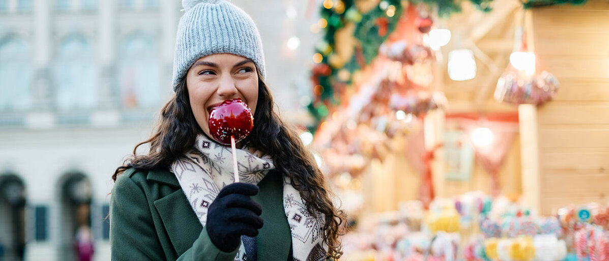 Apfelsorten für Allergiker: Wieso funktionieren die Äpfel anders als alte Apfelsorten? Eine Frau auf einem Weihnachtsmarkt beißt in einen kandierten Apfel.