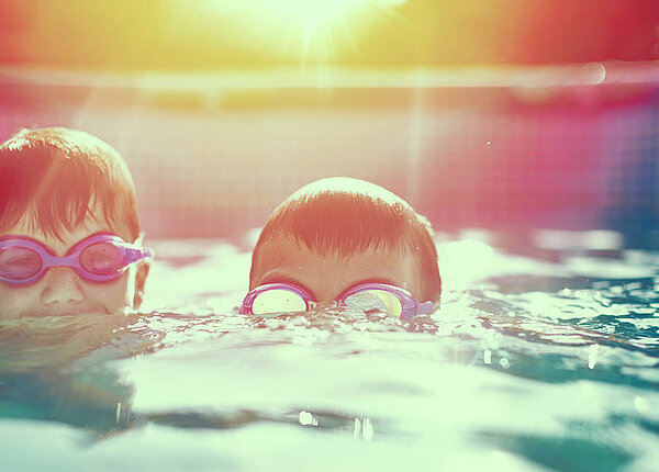 Augen gereizt durch Chlorwasser nach dem Schwimmbad Zwei Jungen im Freibad: Beide haben das Gesicht halb über, halb unter Wasser und tragen eine Schwimmbrille.