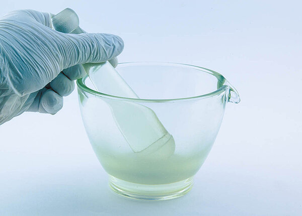 Individualrezeptur: Wann ist die richtige Herstellungstechnik das Rührsystem? Wann eignet sich das Rühren per Hand besser? Eine Fantaschale und ein Pistill aus Glas, mit denen eine behandschuhte Hand eine weiße, opake, halbfeste Zubereitung anrührt