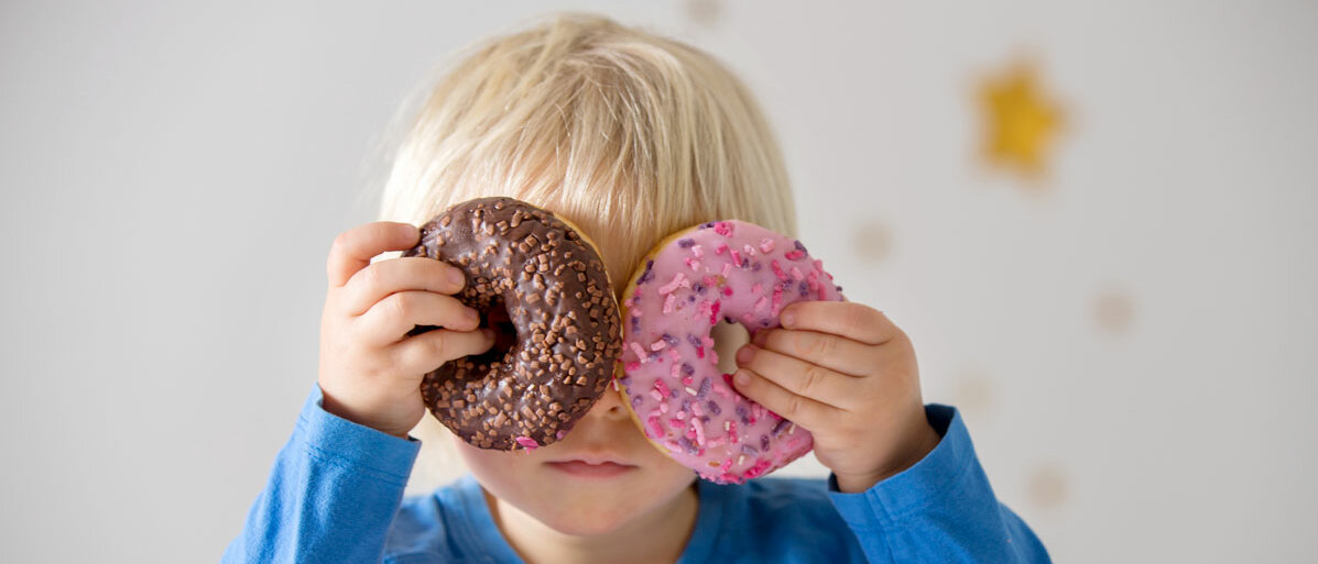 Kleiner Junge haelt zwei Donuts vor die Augen