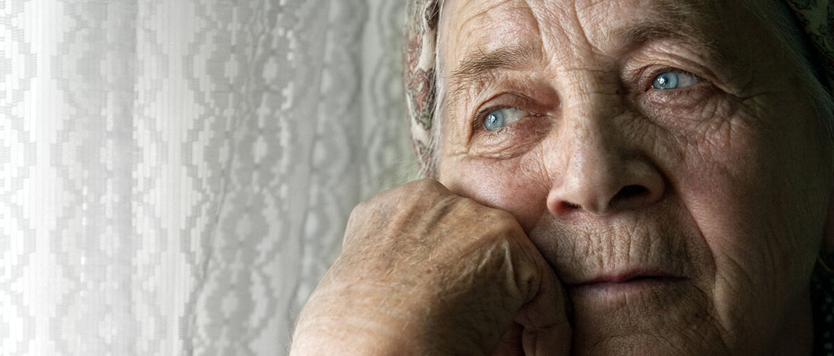 Eine alte Frau stützt das Gesicht auf die Hand und schaut aus dem Fenster.