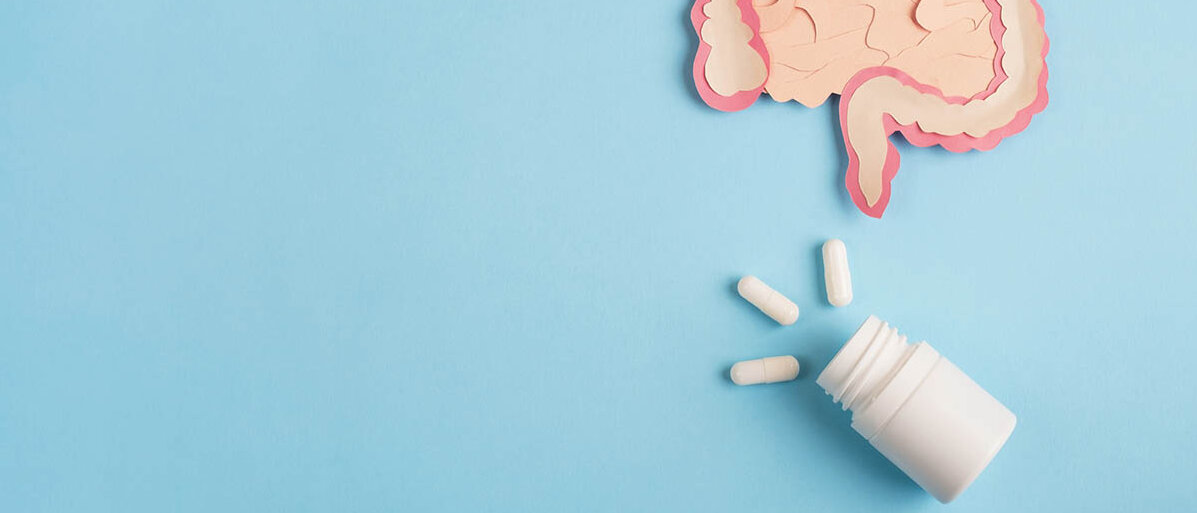 Flatlay: Scherenschnitt des Dick- und Dünndarms, darunter eine Dose, aus der drei Kapseln herausschauen.