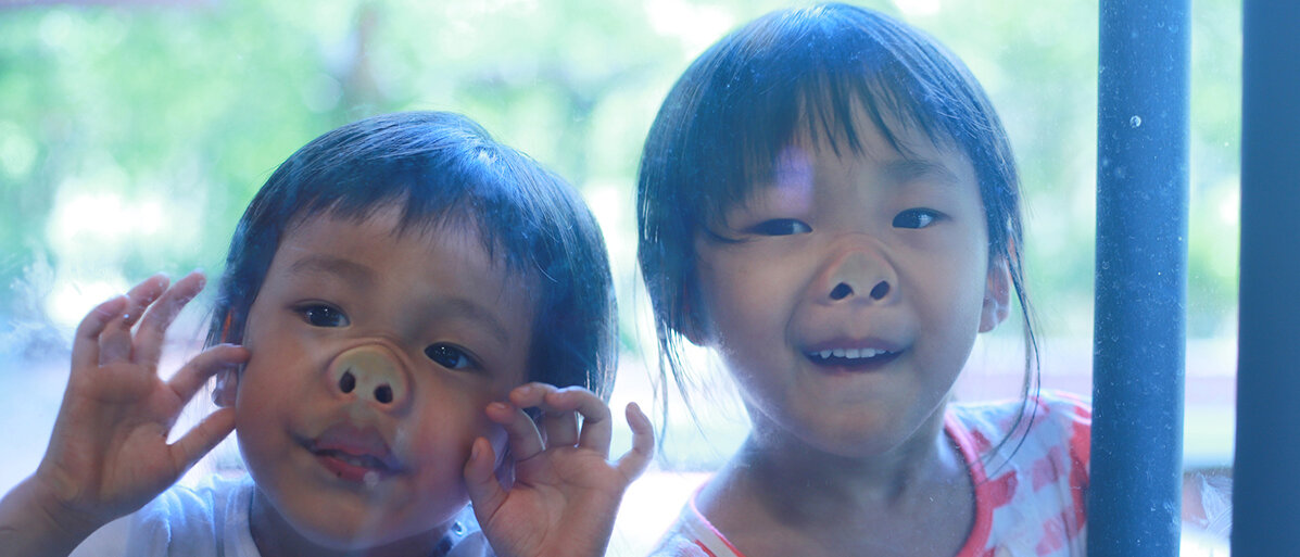 zwei Kinder drücken sich die Nasen an einem Fenster platt