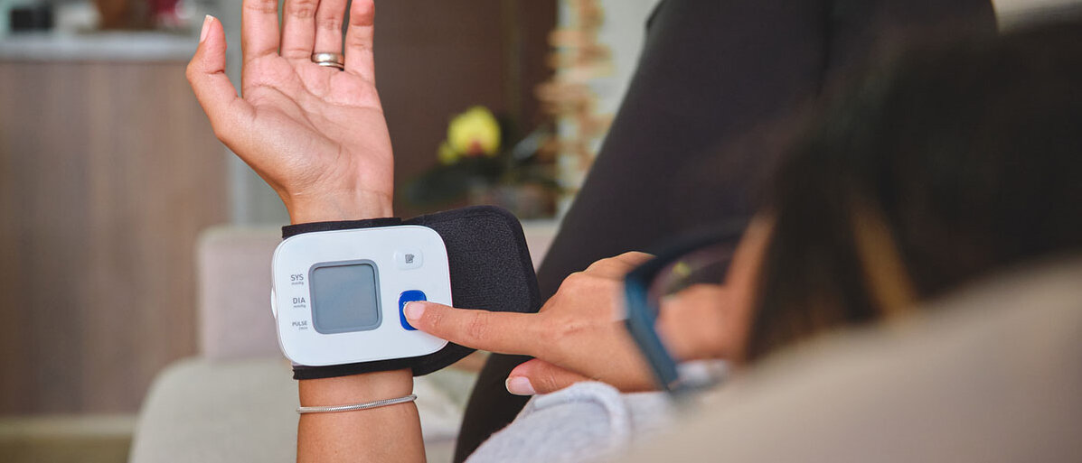 Sitzende Frau von hinten mit angewinkelten Beinen misst Blutdruck